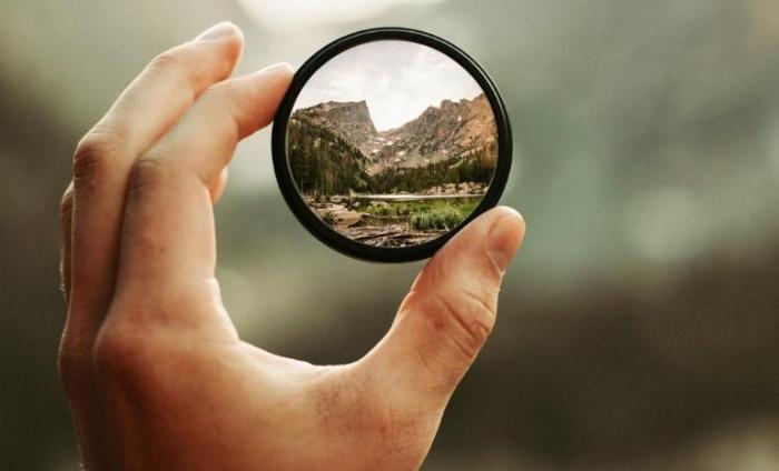A magnifying glass being held up to the mountains to focus in on the bigger picture further away 