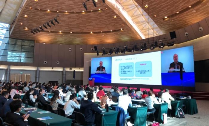 Photo of male speaker on big digital screens delivering a talk to the audience at a forum in Shanghai