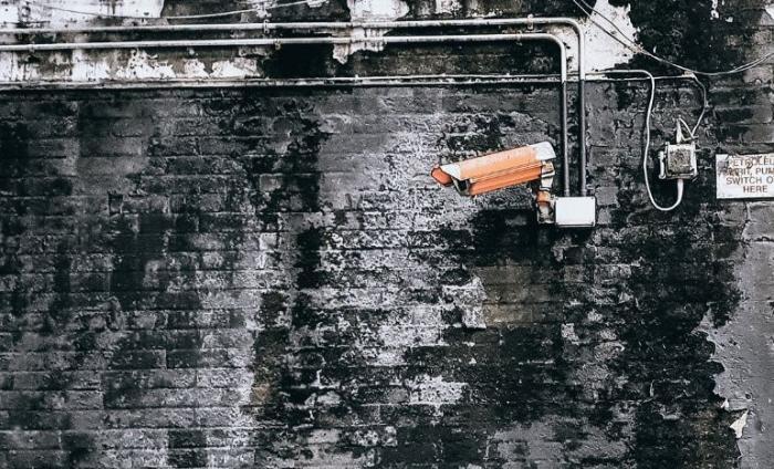 A grey wall on the street with a CCTV camera