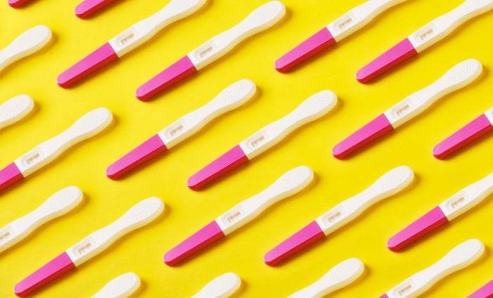 Multiple pregnancy tests lined up on a yellow background