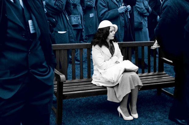 Woman in all white sat on a bench with people stood around. Blue hue to the picture.